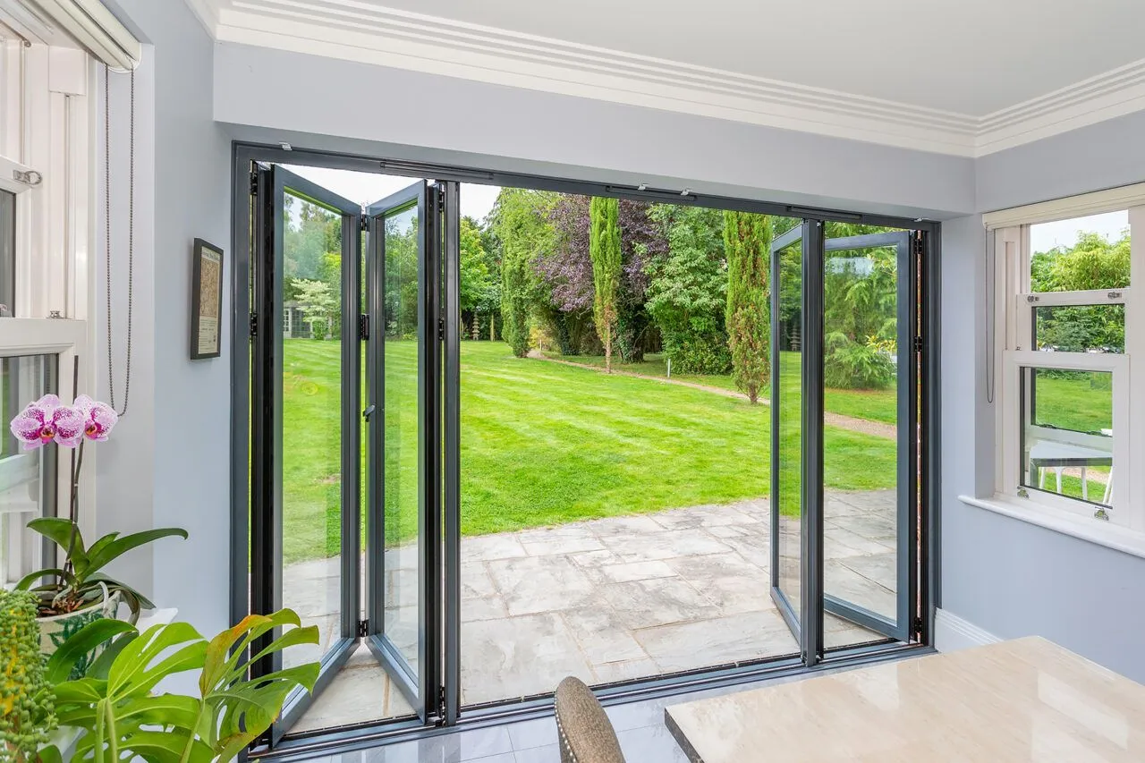 Anthracite-framed bifold doors folded open from a bright sitting room onto a garden